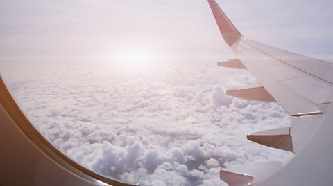 The wing of an airplane among white clouds as seen from a plane window.