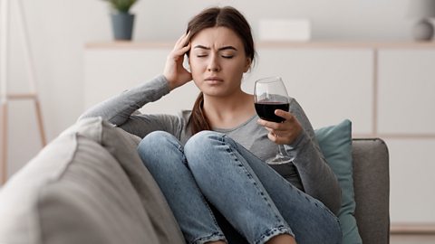 person sits on the sofa with a headache while holding a glass of red wine