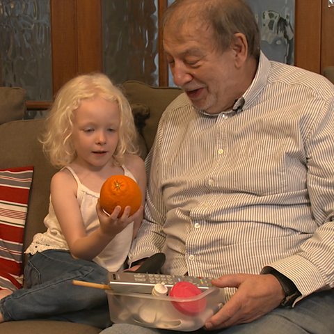 Little girl and granddad on the sofa, holding an orange.