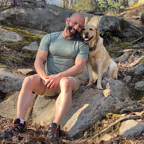 A picture of Magnus the therapy dog and his owner Brian sitting on a rock together.