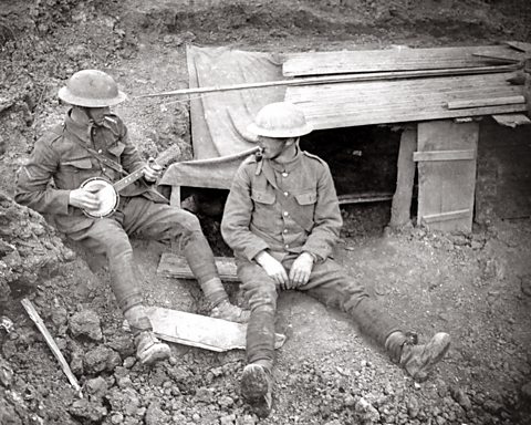 A British soldier plays a banjo outside a trench dugout on the Western Front, 1916.