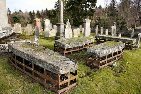 Four graves surrounded by iron and stone cages in a cemetery. 