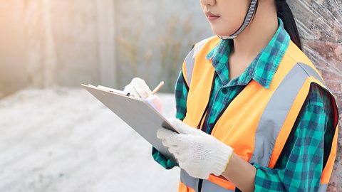 An image of a woman in hi-vis clothing writing on a clipboard.