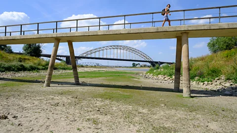 Thierry Monasse/Getty Images Woman walking across bridge above dry riverbed (Credit: Thierry Monasse/Getty Images)