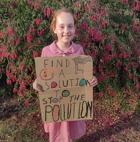 Rosa holds up her homemade sign that says "find a solution to stop the pollution"