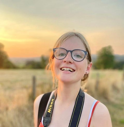 Matilda smiles to the camera in the wild. She has a camera strap around her neck so she can take photos of nature