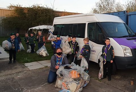 A group of children show off their litter picking skills in front of a van. They are holding litter pickers as well as bags full of rubbish.