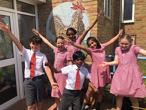 Six students smile and pose in front of their school.