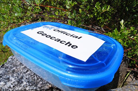 A box with a blue lid labelled 'Official Geocache' 