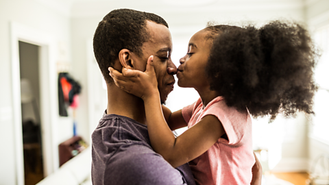 little girl kisses her dad, who is holding her, on the nose