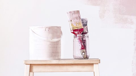 A semi-painted wall and emulsion paint with brushes in a jar.