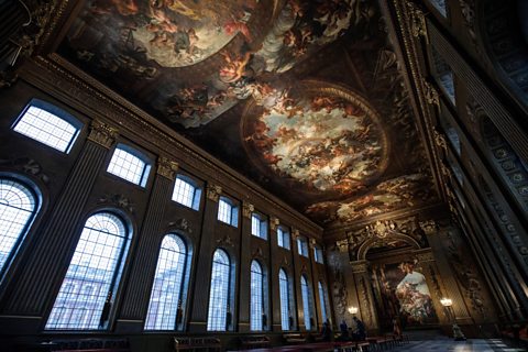 A long dark room with arched windows along each side. Focus is on the ceiling, which is painted with figures and the heavens.