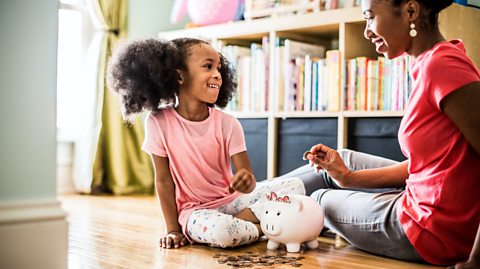 A mum and daughter sat together filling a piggy bank