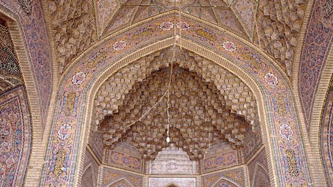 A photo of a tiled archway, wall and ceiling. The tiles are predominantly pink and yellow with floral designs.