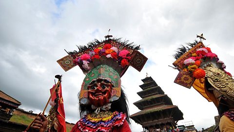 A man wearing a black hooded cape, with his face painted as a skull, attending a Gai Jatra parade.