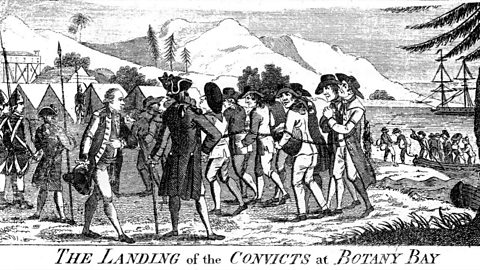 Illustration of convicts landing at Botany Bay, Australia. They are chained and walking in front of the guards. In the background other smaller ships are landing. 