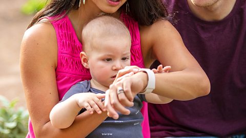 A baby boy looking at his mum's wristwatch.