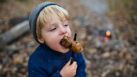 child eating a jacket potato with a bonfire in the background