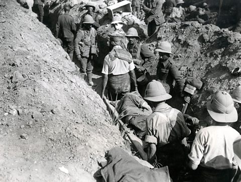 Injured British soldiers being carried by stretcher down a busy communication trench in Mesopotamia (now Iraq), WW1.