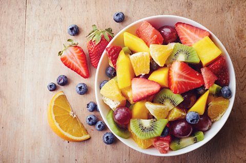 A bowl of fruit, and some placed on the table around it.