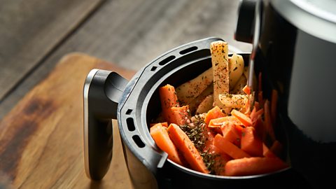 An airfryer with root veg - including carrots and potatoes - in the basket