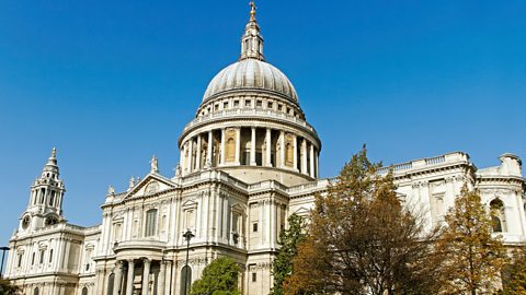 A contemporary photograph of St Paul's Cathedral from the front facade with some trees in front of it and a blue sky in the background. 