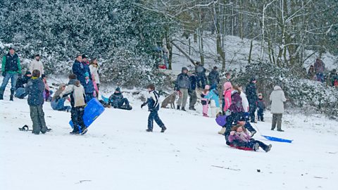 Daoine a' ruith mun cuairt agus a' sleidseadh san t-sneachd