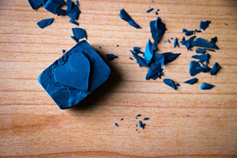 A blue rubber stamp carved with a heart shape sitting on a wooden background