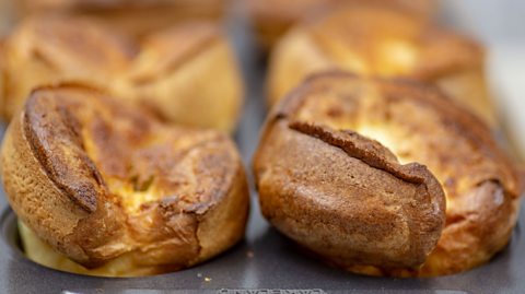 A grey baking tray filled with golden brown Yorkshire puddings