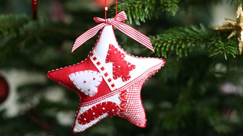 A red and white textile star Christmas tree decoration, hung from a branch