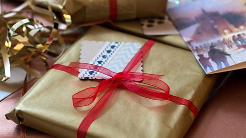 A square Christmas present wrapped in gold paper and tied with a red ribbon