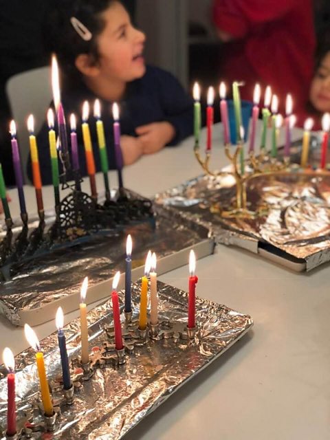 2 young girls sat at a table with 3 menorahs.