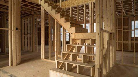 House construction interior with exposed framing, wooden frame of stairs, plywood floors