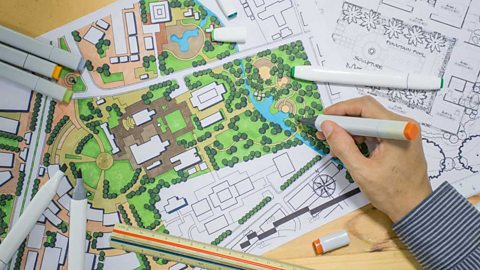 Closeup of man's hand drawing a plan for an outdoor space with markers, rulers on a table