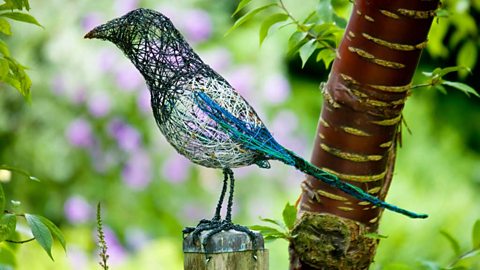 Wire sculpture of a magpie in profile perched on a post beside a tree