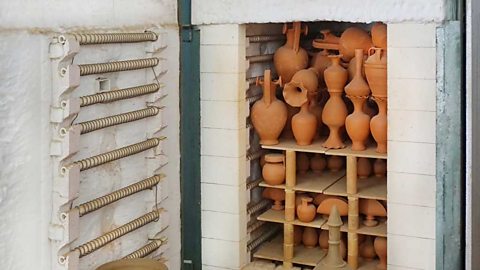 A large stone kiln with the door open. Shelves of orange pots inside