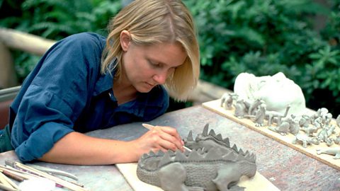 A woman in a blue shirt making a dragon out of clay with a wooden tool