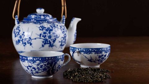 A blue and white teapot and cup on a wooden table and a pile of loose leaf tea