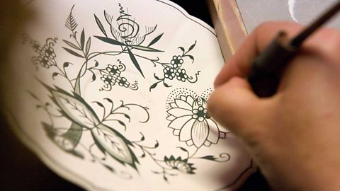 A hand painting green floral designs on a ceramic plate