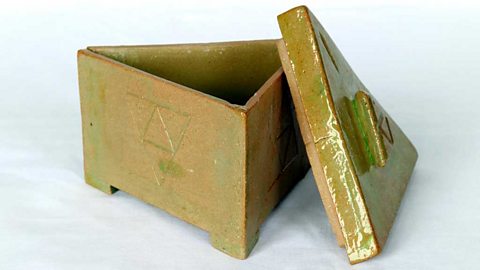 A yellow-brown triangular box and lid with triangle designs on its faces