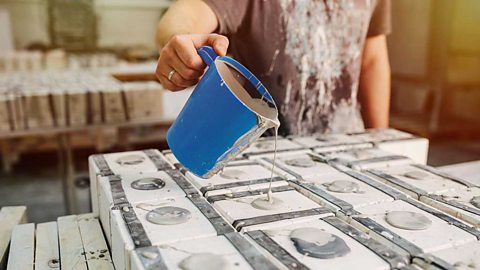 A hand holding a blue jug and pouring liquid clay into holes in the tops of white boxes