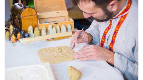 A man using a metal pen-like tool to carve designs on a small clay panel