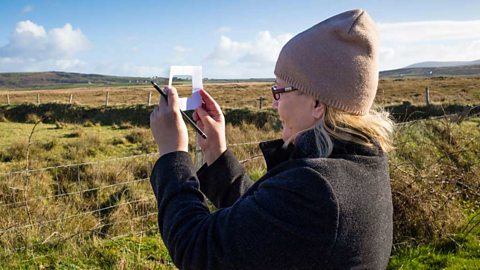 Woman in a field holding a pencil and a paper frame