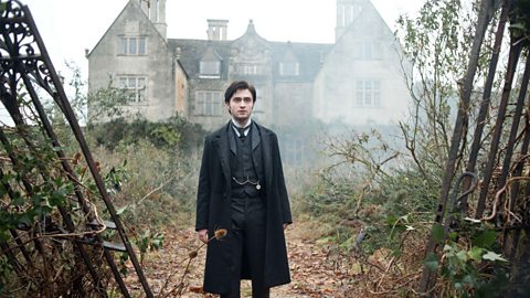 An image of actor Daniel Radcliffe as Arthur Kipps standing in front of Eel Marsh House in the 2012 film adaptation of the novel