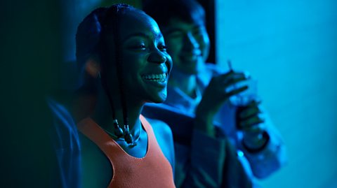 Two people smile under a blue light.