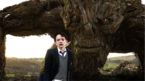 A still from the 2016 film version of A Monster Calls. Conor is in the foreground looking distressed. The giant monster looms intensely behind him.