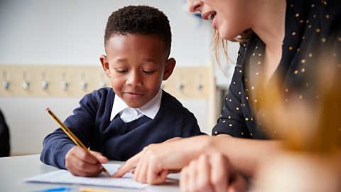 A young boy at primary school learning to write with his teacher.