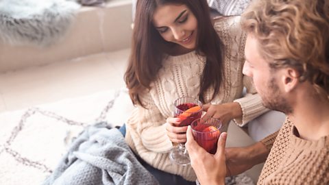 A couple have a winter warming drink with a blanket wrapped on them
