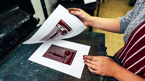 A person lifting a printed piece of paper off a design.