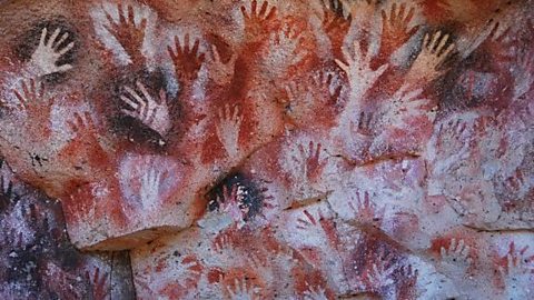 Handprints on red and orange rock at Cueva de la Manos in Argentina.